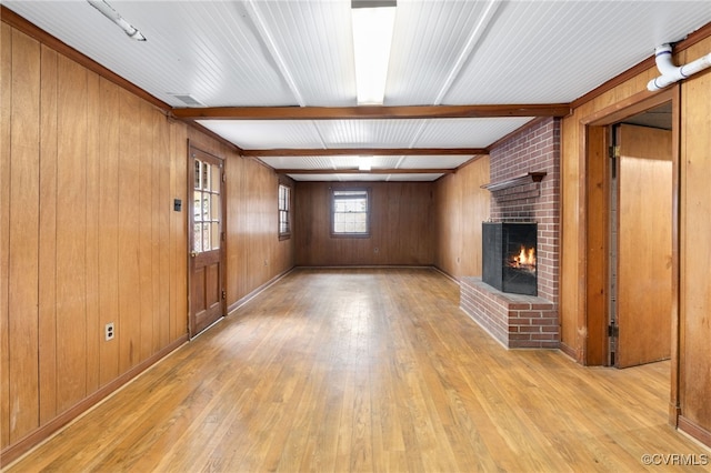 unfurnished living room with a brick fireplace, wooden walls, beamed ceiling, and light wood-type flooring