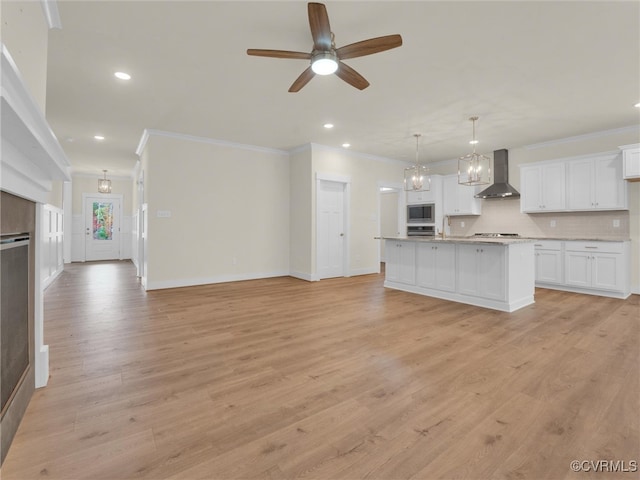 kitchen with light wood-type flooring, wall chimney exhaust hood, white cabinetry, hanging light fixtures, and an island with sink