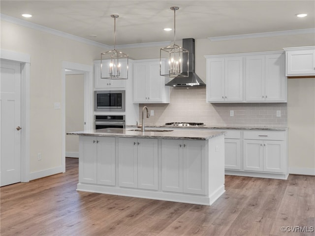 kitchen with a kitchen island with sink, white cabinets, stainless steel appliances, and wall chimney range hood