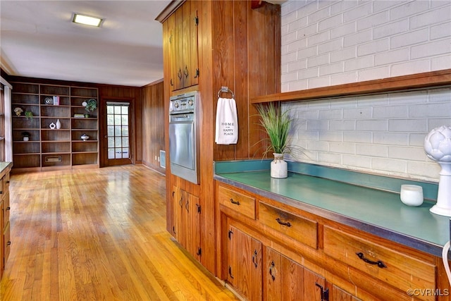 kitchen featuring light hardwood / wood-style floors, wood walls, oven, and backsplash