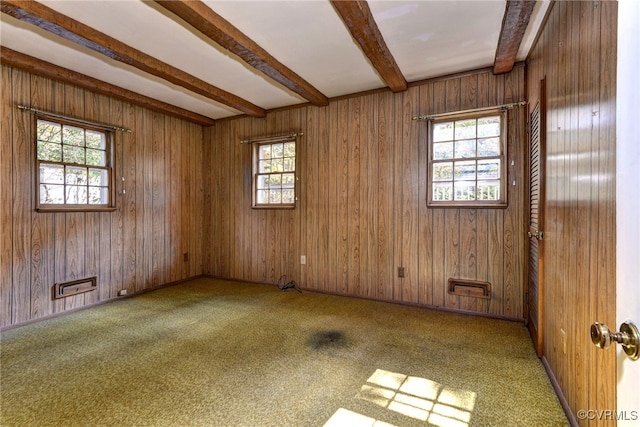 carpeted empty room with beamed ceiling, wooden walls, and plenty of natural light