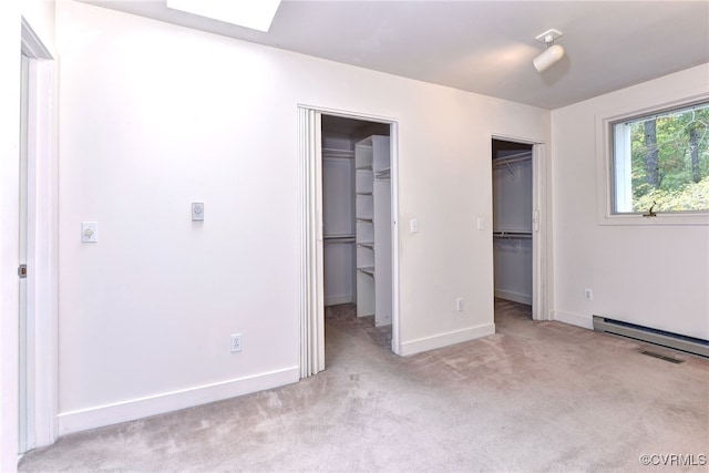 unfurnished bedroom with a skylight, a spacious closet, light colored carpet, and baseboard heating