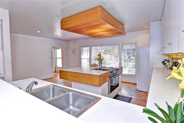 kitchen with high end stove, sink, white cabinetry, white fridge, and light hardwood / wood-style floors