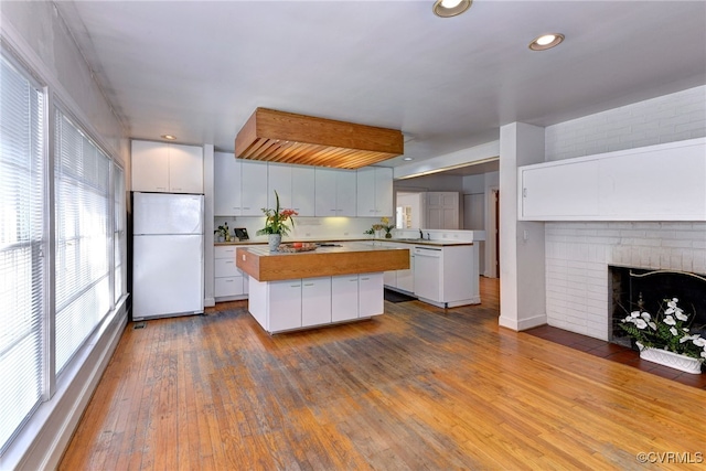 kitchen featuring white fridge, hardwood / wood-style flooring, a kitchen island, and white cabinets