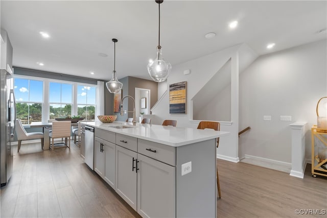 kitchen featuring sink, dishwasher, hanging light fixtures, light hardwood / wood-style floors, and a center island with sink