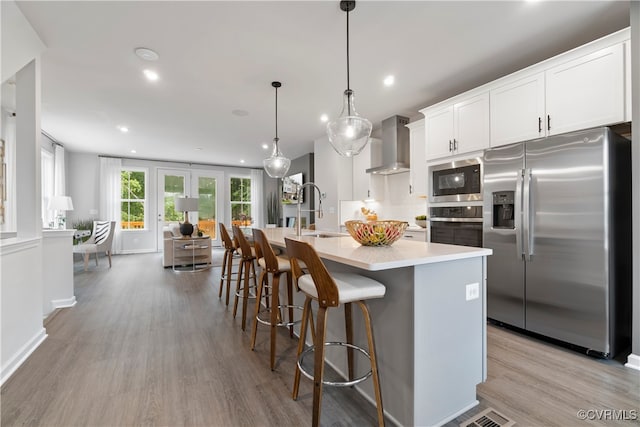 kitchen featuring white cabinets, hanging light fixtures, sink, wall chimney exhaust hood, and stainless steel appliances