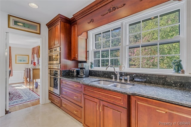 kitchen with sink, double oven, dark stone counters, crown molding, and light tile patterned floors