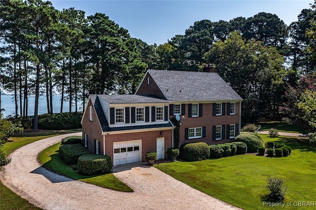 colonial-style house featuring a water view, a front lawn, and a garage