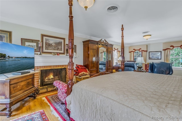 bedroom with light hardwood / wood-style floors, ornamental molding, and a brick fireplace