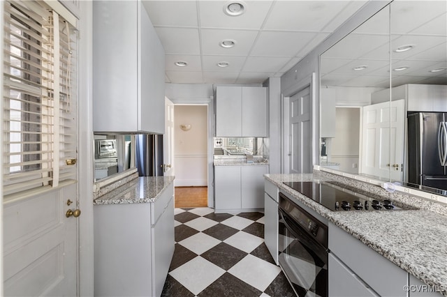 kitchen featuring black appliances, a paneled ceiling, white cabinets, and light stone counters