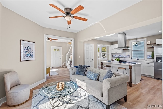 living room with ceiling fan, sink, and light wood-type flooring