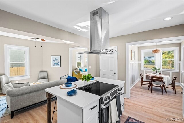 kitchen featuring white cabinetry, island range hood, a breakfast bar, stainless steel range with electric cooktop, and light wood-type flooring