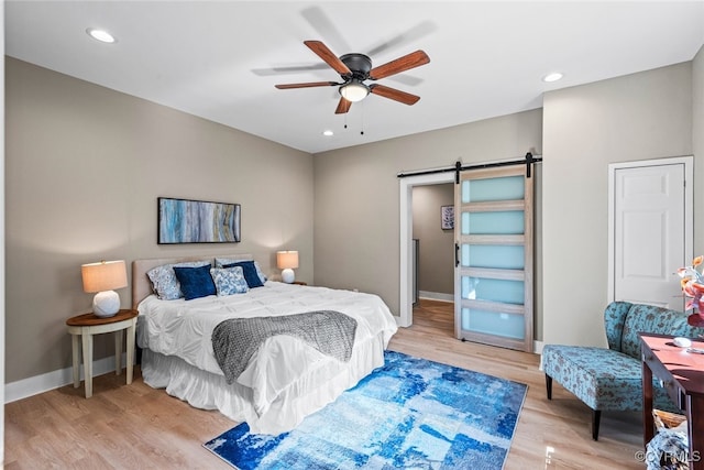 bedroom featuring ceiling fan, a barn door, and light hardwood / wood-style floors