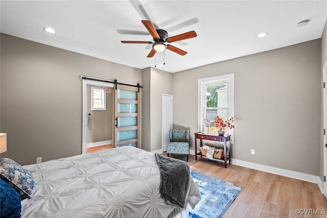 bedroom with a barn door, light hardwood / wood-style floors, and ceiling fan