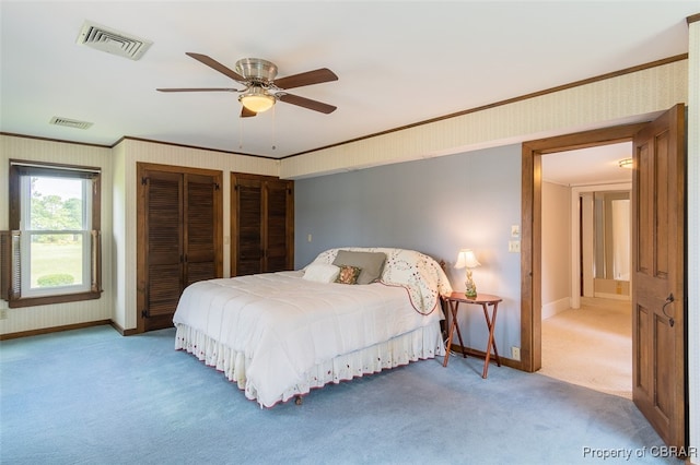 carpeted bedroom with ornamental molding, two closets, and ceiling fan