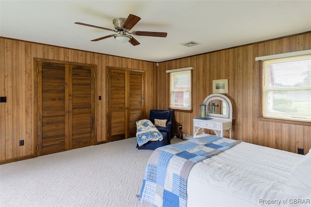 bedroom with wood walls, multiple closets, multiple windows, and ceiling fan