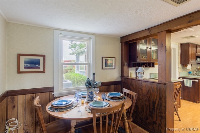 dining space with wood walls, a textured ceiling, and light wood-type flooring