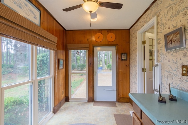 doorway with crown molding, ceiling fan, and wood walls