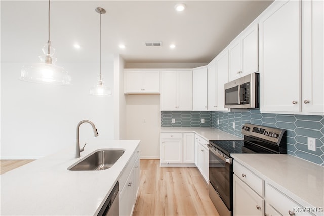 kitchen with sink, light wood-type flooring, white cabinetry, stainless steel appliances, and decorative light fixtures