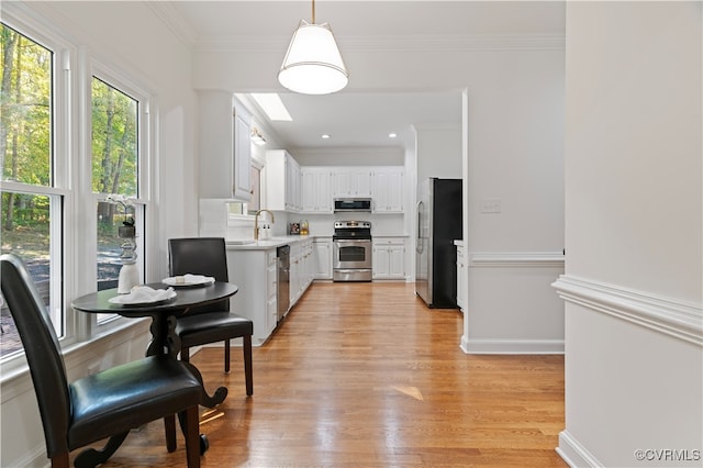 kitchen with white cabinets, appliances with stainless steel finishes, light hardwood / wood-style flooring, pendant lighting, and sink