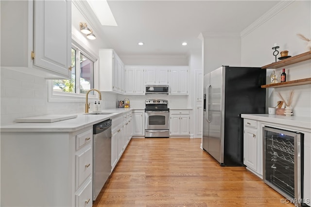 kitchen featuring wine cooler, appliances with stainless steel finishes, white cabinetry, light hardwood / wood-style floors, and sink