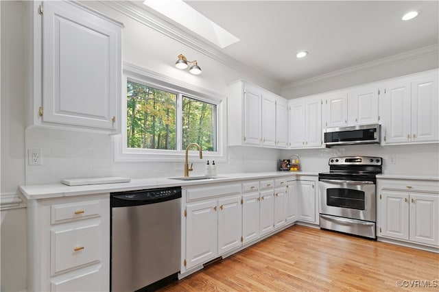 kitchen with appliances with stainless steel finishes, white cabinets, sink, and light wood-type flooring