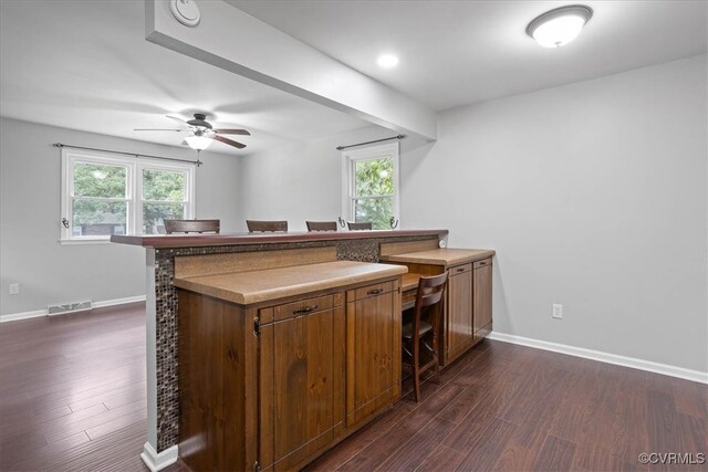 kitchen with kitchen peninsula, dark wood-type flooring, a kitchen bar, and plenty of natural light