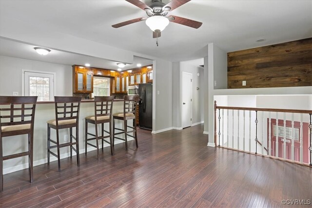 kitchen featuring dark wood-type flooring, ceiling fan, a breakfast bar, and black refrigerator