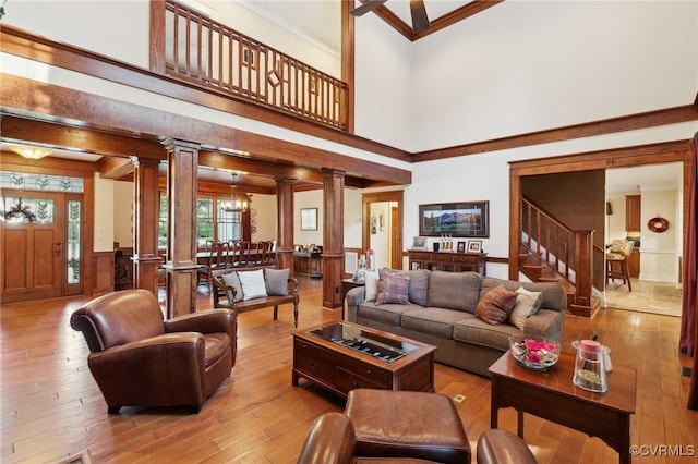 living room with a high ceiling, beamed ceiling, decorative columns, a notable chandelier, and light wood-type flooring