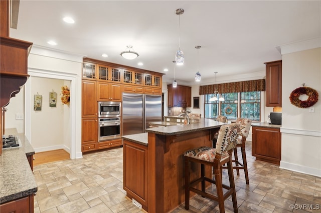 kitchen featuring a center island with sink, high end refrigerator, dark stone countertops, crown molding, and decorative light fixtures