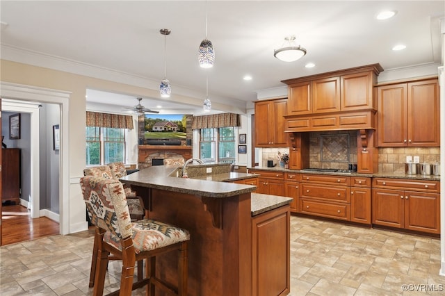 kitchen with decorative backsplash, an island with sink, ceiling fan, ornamental molding, and pendant lighting