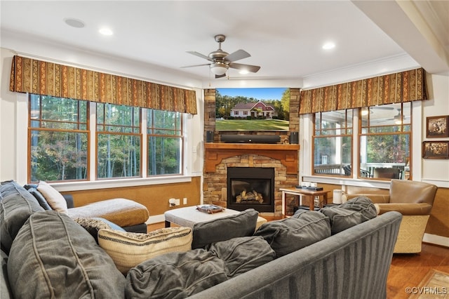 living room featuring hardwood / wood-style floors, a baseboard radiator, ceiling fan, ornamental molding, and a stone fireplace