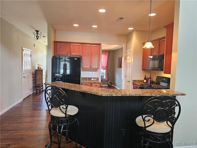 kitchen with a kitchen bar, dark hardwood / wood-style floors, hanging light fixtures, and black appliances