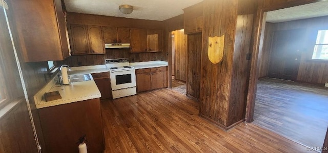 kitchen featuring dark wood-type flooring, electric stove, wood walls, and sink