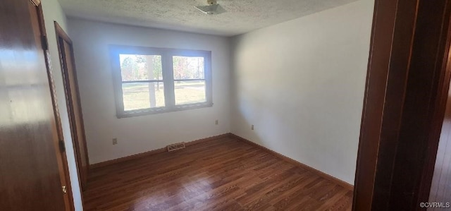 spare room with a textured ceiling and dark hardwood / wood-style flooring