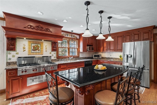 kitchen featuring stainless steel appliances, dark stone counters, a center island, decorative light fixtures, and light hardwood / wood-style floors