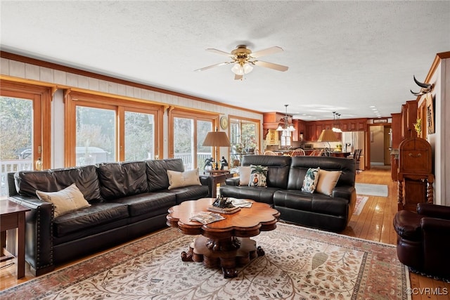 living room featuring ceiling fan, a textured ceiling, wood walls, ornamental molding, and light hardwood / wood-style floors