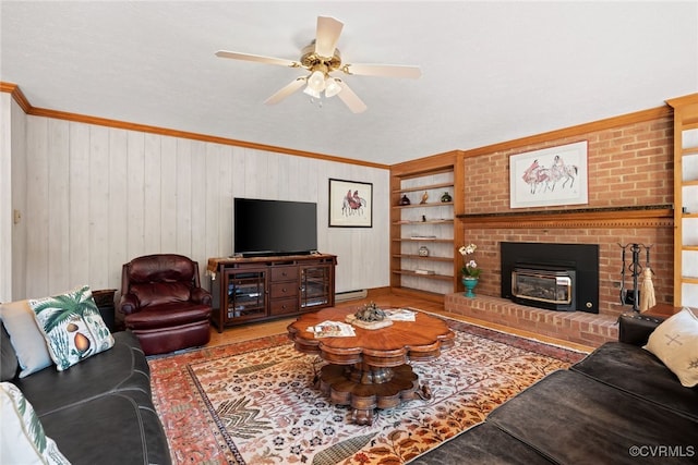 living room with ceiling fan, wood walls, a fireplace, built in shelves, and crown molding