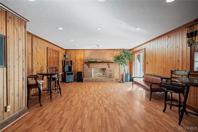 living room with a textured ceiling, light wood-type flooring, wood walls, a fireplace, and crown molding