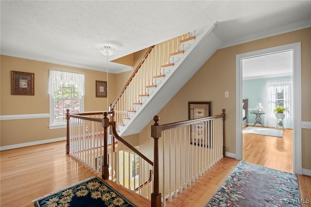 staircase featuring a textured ceiling, ornamental molding, and hardwood / wood-style floors