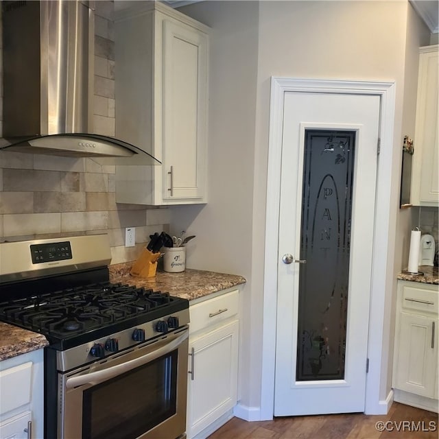 kitchen with wall chimney range hood, stainless steel gas range oven, dark stone counters, and backsplash