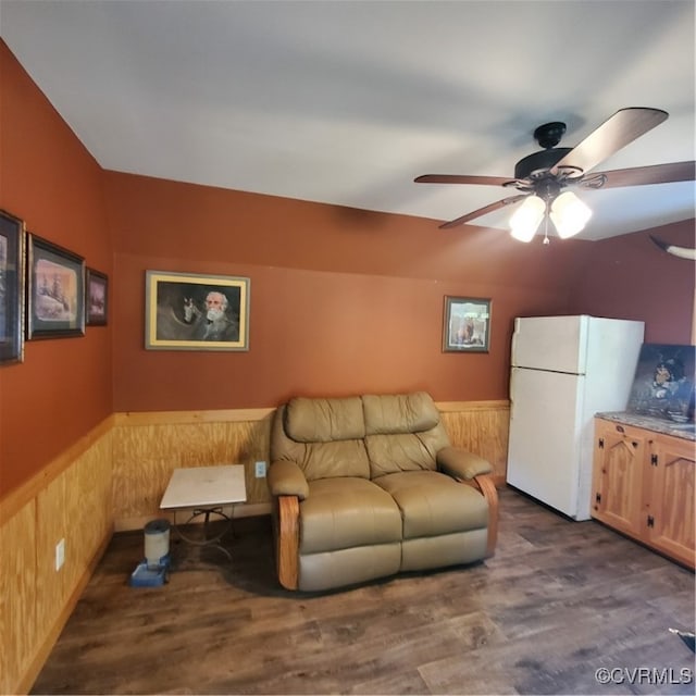 living room with wooden walls, dark wood-type flooring, and ceiling fan