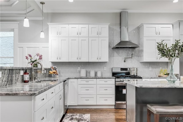 kitchen with wall chimney range hood, white cabinetry, ornamental molding, sink, and stainless steel appliances