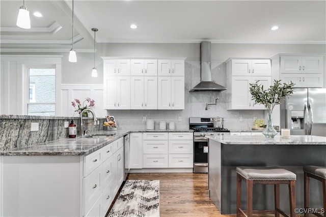 kitchen with wall chimney range hood, stainless steel appliances, crown molding, sink, and white cabinets