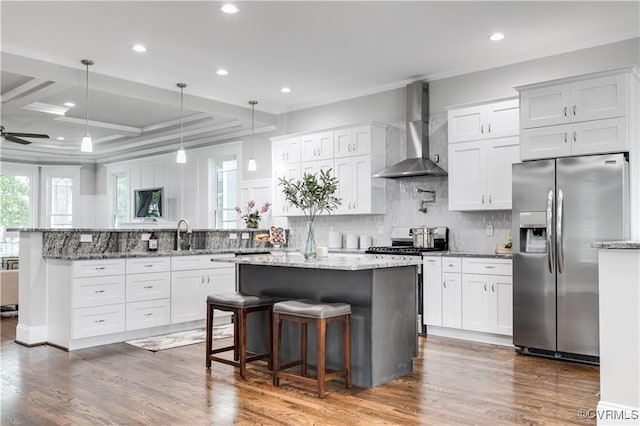 kitchen featuring wall chimney range hood, white cabinets, stainless steel appliances, and plenty of natural light