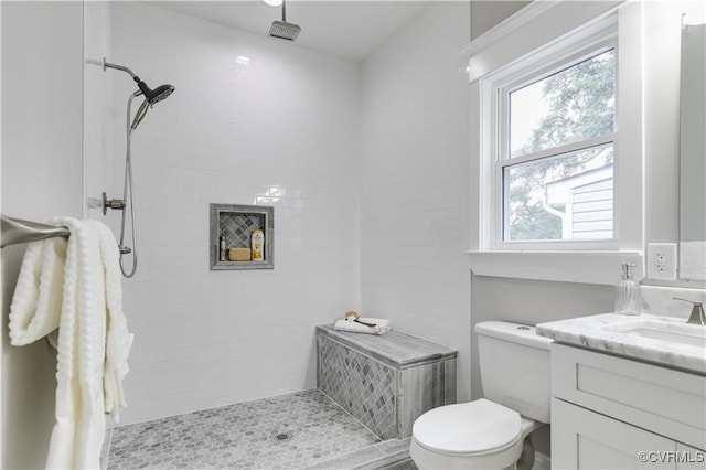 bathroom with a tile shower, toilet, and vanity