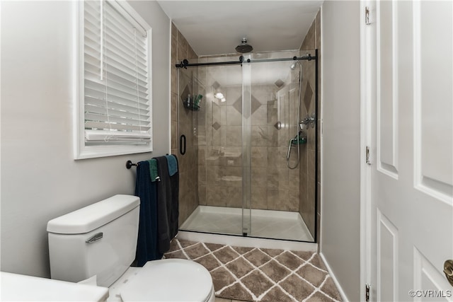 bathroom featuring a shower with door and toilet