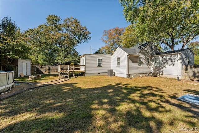 back of property with central AC, a wooden deck, a storage shed, and a yard