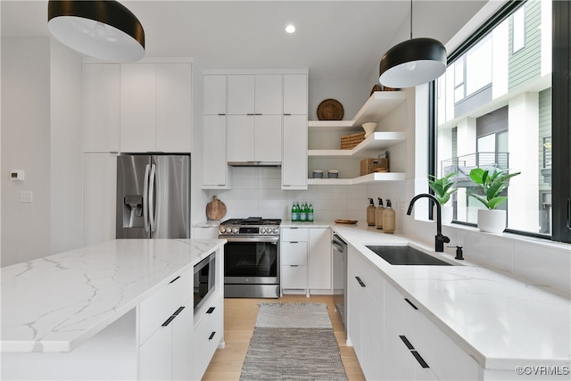 kitchen featuring white cabinets, sink, light stone countertops, appliances with stainless steel finishes, and decorative light fixtures