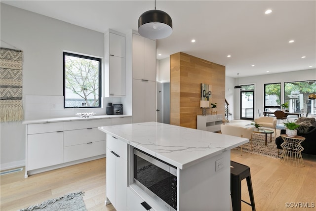 kitchen with white cabinets, a wealth of natural light, decorative light fixtures, and stainless steel microwave